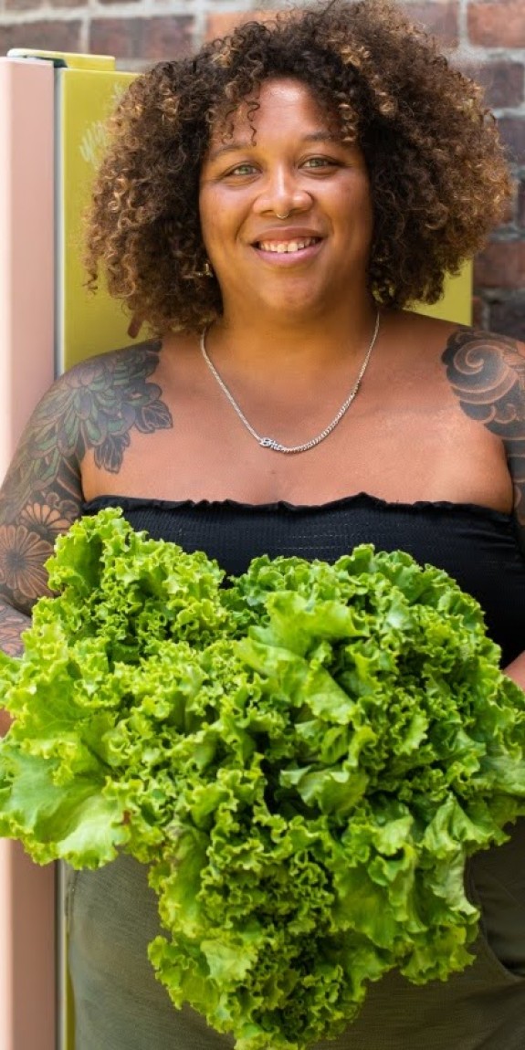 A person standing in front of a community fridge holding lettuce 